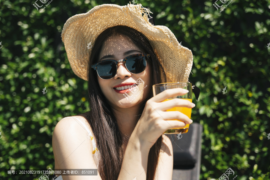 亚洲旅行家妇女的画像戴太阳镜和帽子在夏天享受橙汁。