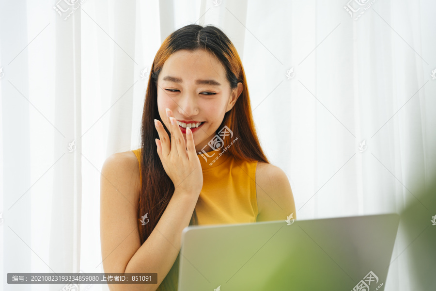 在家里用笔记本电脑工作的美丽年轻的亚洲女人。