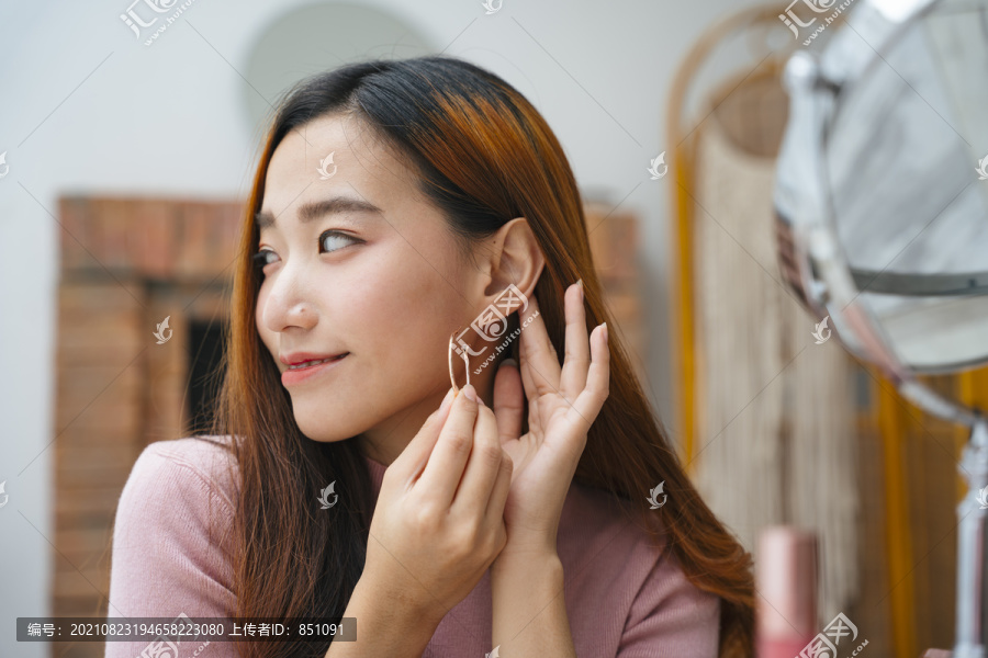 美丽的亚洲女人戴着耳环对着镜子。