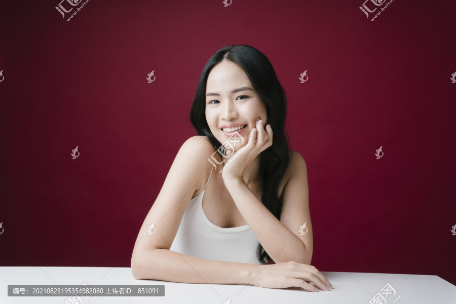 美丽的亚洲女人的画像，完美的自然皮肤护理微笑着对着隔离在红色背景上的相机。