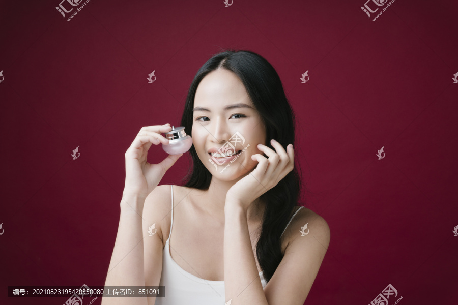 一位年轻美丽的女士手持一罐隔离在红色背景上的奶油化妆品的肖像。