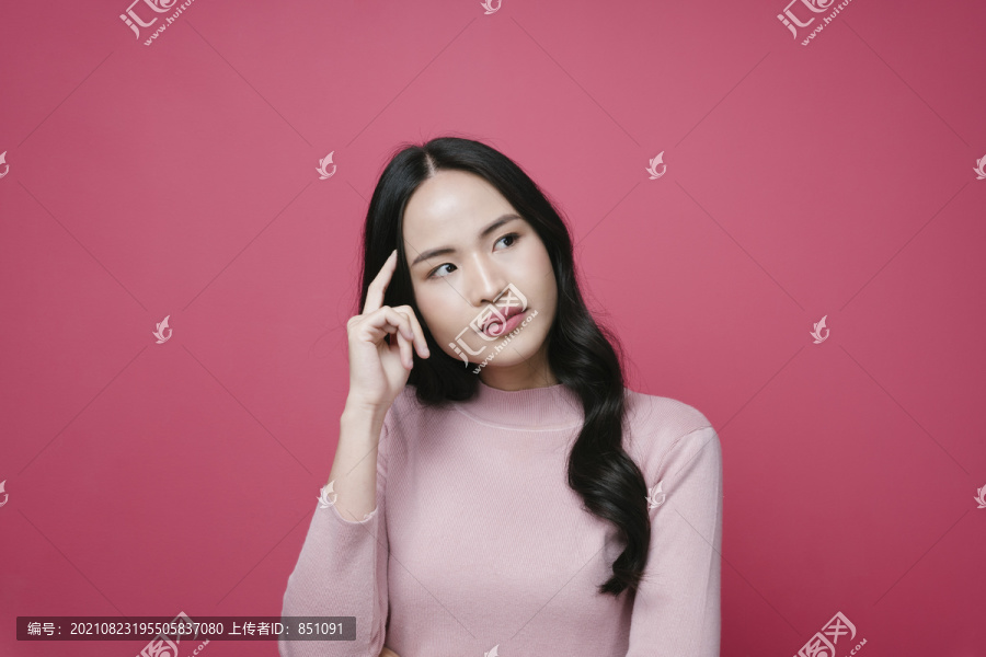 粉红色背景上，年轻亚洲女性的肖像，表情深思熟虑。