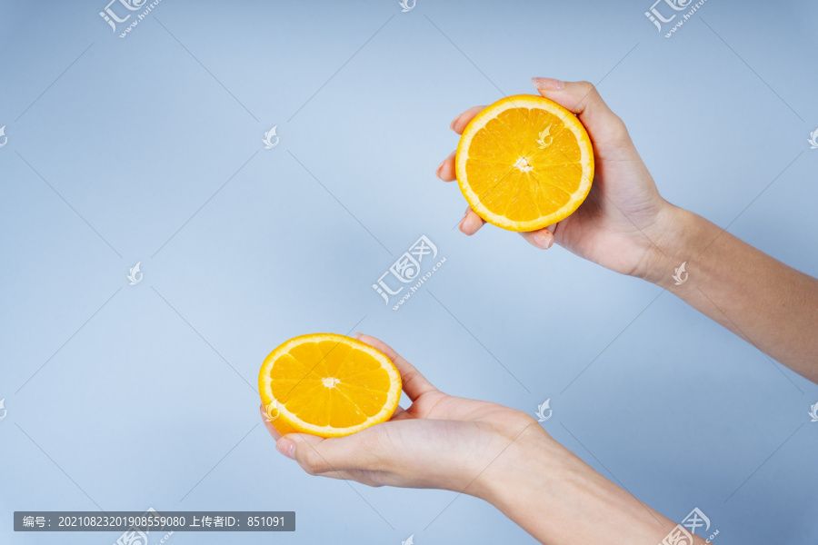 一个女人的两只手拿着蓝色背景上的一片橘子。