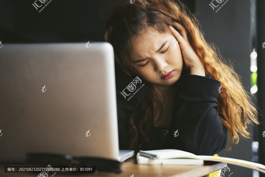 无聊的亚洲女人厌倦了学习，坐在校园里摆着头痛的姿势。