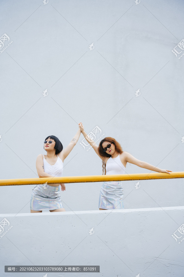 在阳台上，两位年轻的亚洲女性穿着白色背心，戴着墨镜。