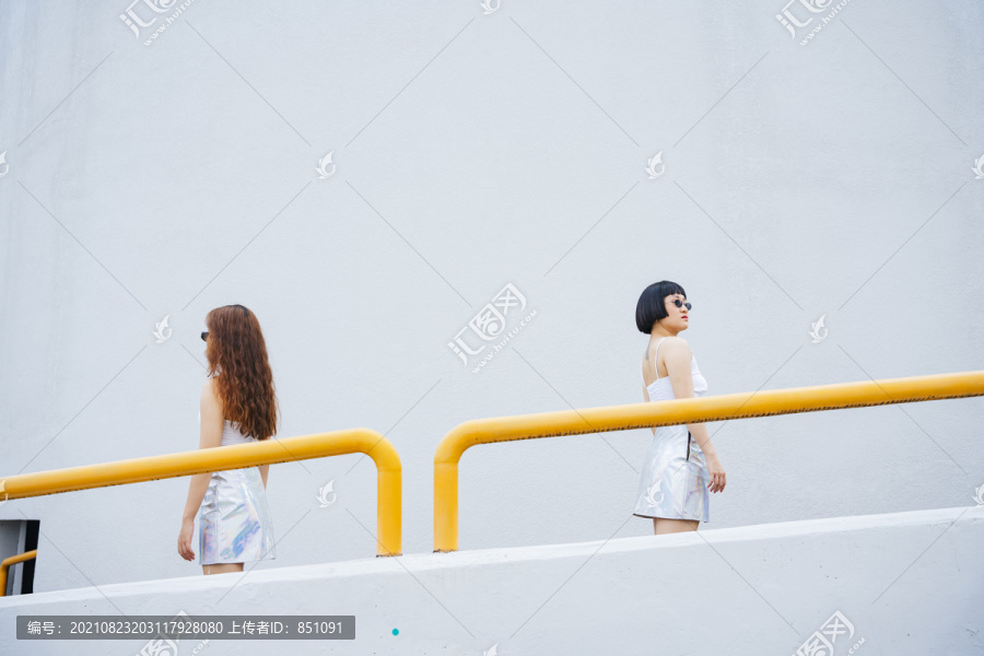 侧视图——两位戴着太阳镜的年轻亚洲女性在城市街道上相互擦肩而过的照片。