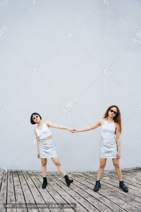 两位身穿白色背心、戴着太阳镜、手牵着手的年轻亚洲女性的肖像。