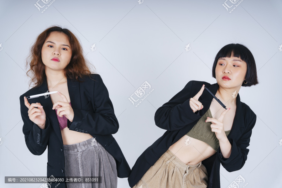 两位穿着黑色夹克套装、白色背景上有一支笔的年轻亚洲商业女性的肖像。