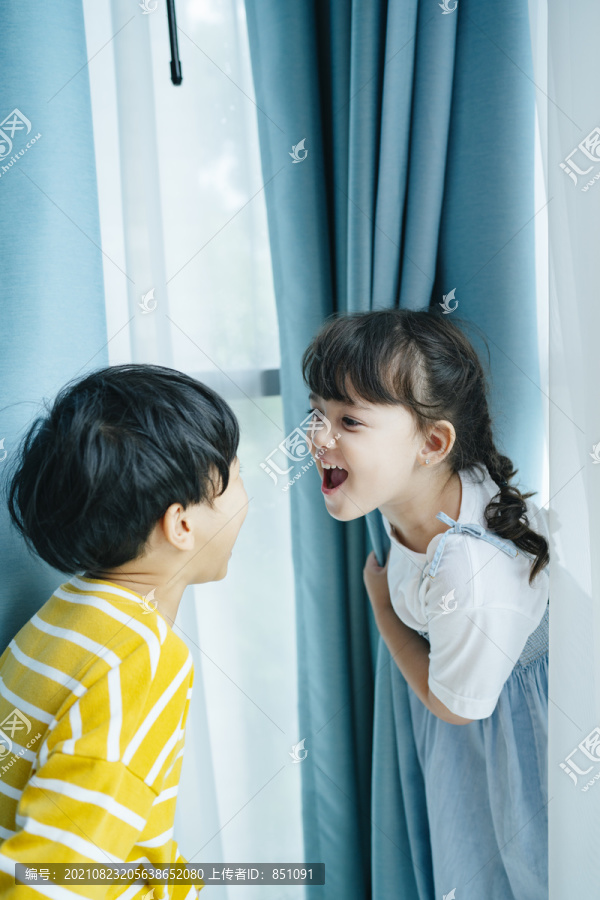 顽皮的男孩和女孩在帘子后面玩得很开心，看着对方的脸。