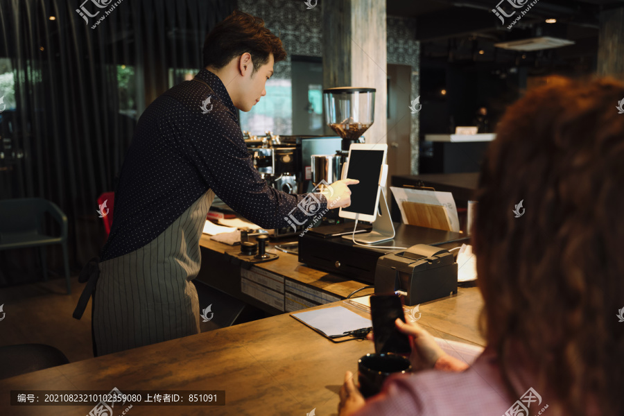 在咖啡馆用数字平板电脑制作食物和账单的酒保。