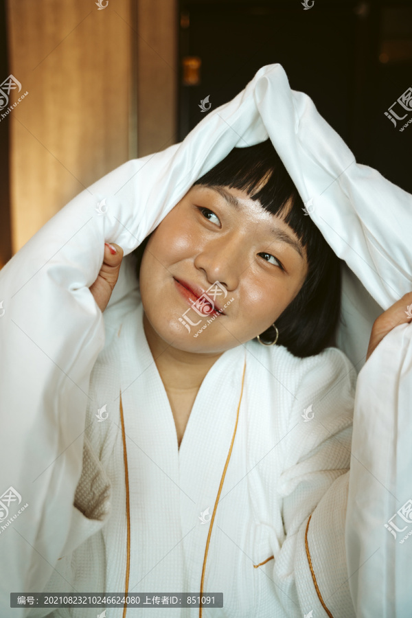 亚洲短发女子在卧室里玩白色毯子。