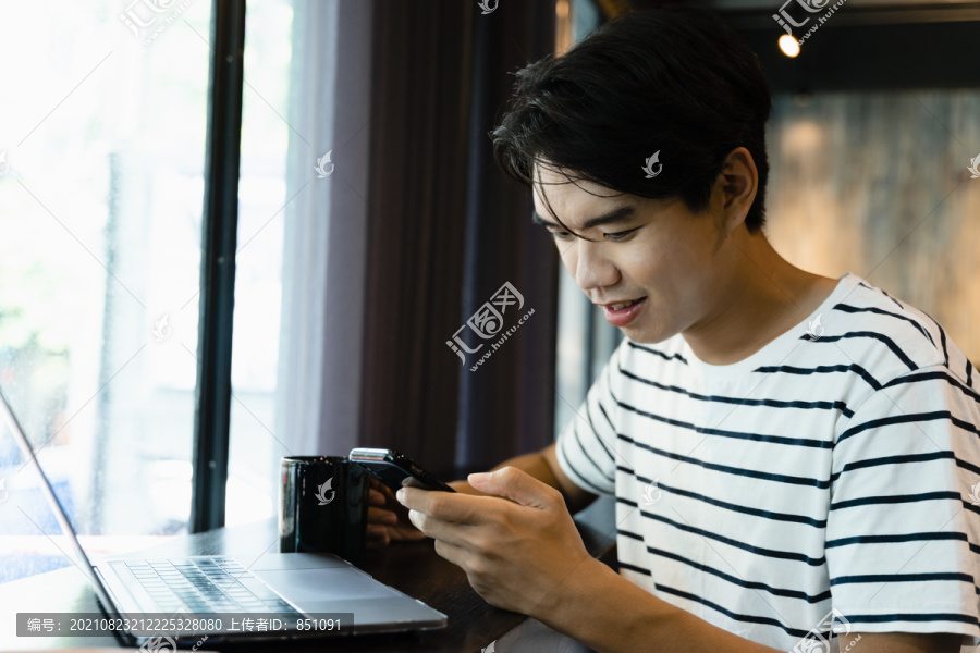 亚裔男子在咖啡馆使用智能手机和笔记本电脑。