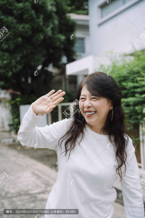 快乐的亚洲老妇人挥手向邻居问好。
