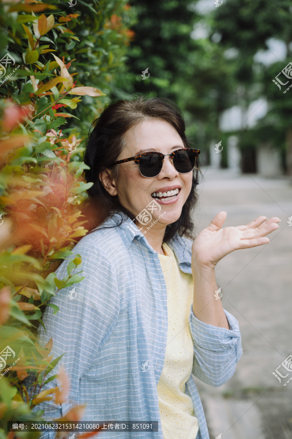 站在植物墙旁戴墨镜的亚洲资深女性肖像。