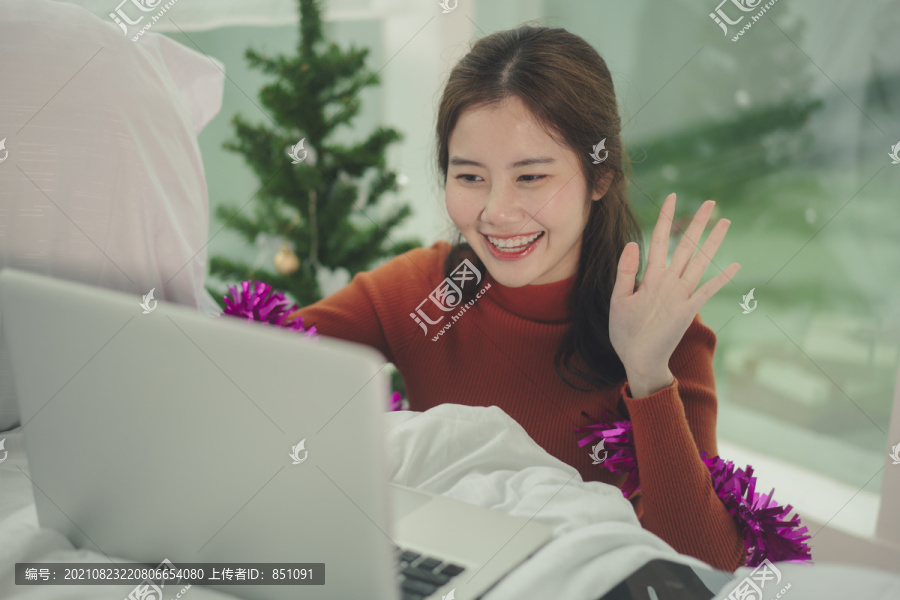 美丽的亚洲年轻女子黑头发在家里用笔记本电脑在线庆祝圣诞节。