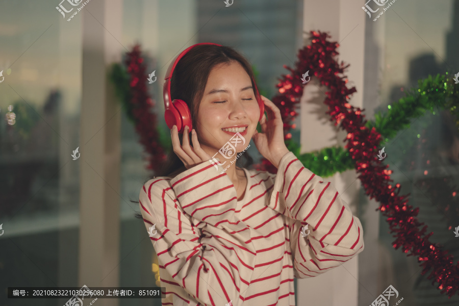 美丽的亚洲年轻女子黑发在圣诞派对上用无线耳机听音乐。