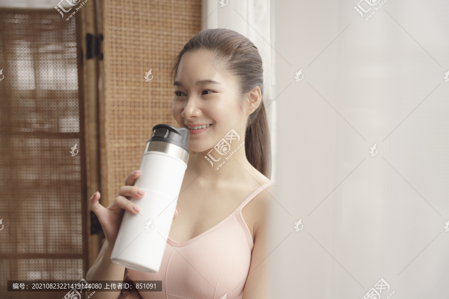 健康的亚洲年轻女性在锻炼后休息，喝瓶装水。