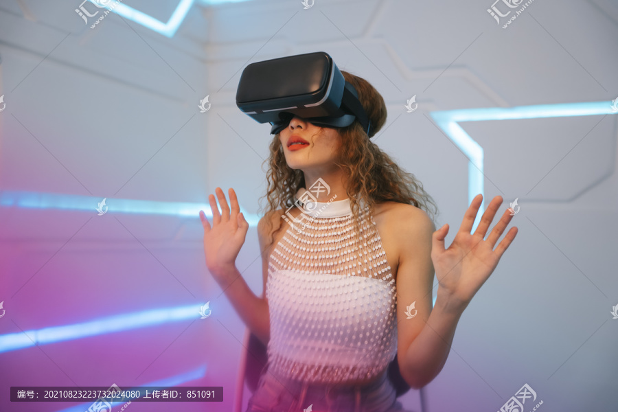 年轻卷发女性的肖像，享受在VR护目镜技术上玩3D游戏。