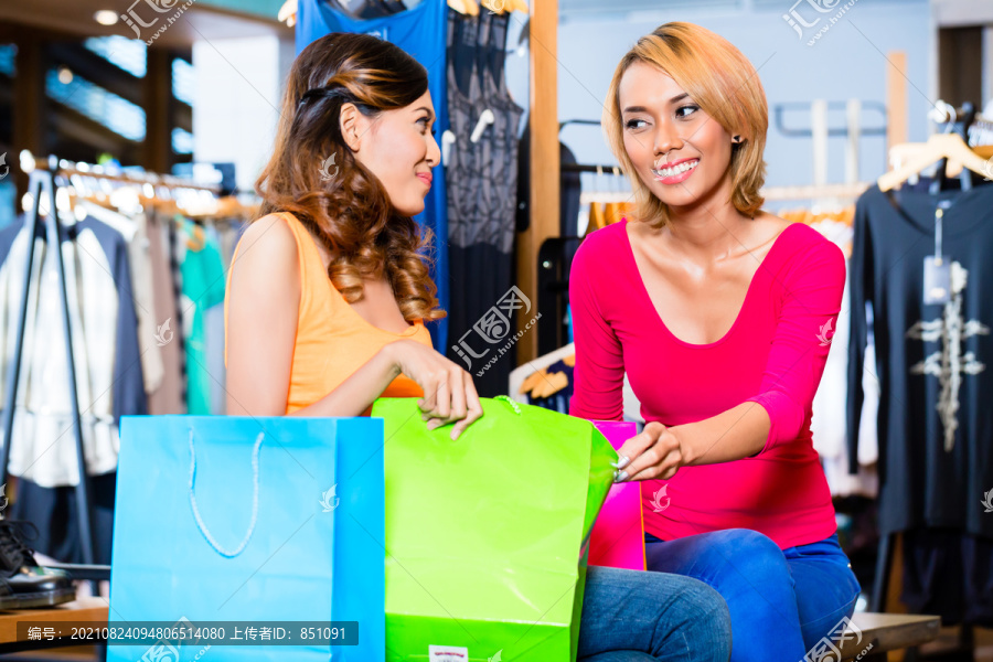 亚洲女朋友在店内时尚购物，相互展示他们的购物袋