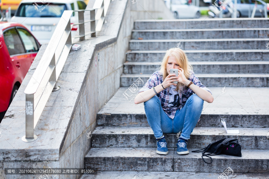 年轻的白人妇女坐在城市户外的楼梯上使用智能手机