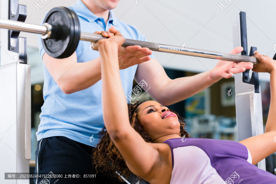 在健身房里，黑人妇女和教练在杠铃上举重健身
