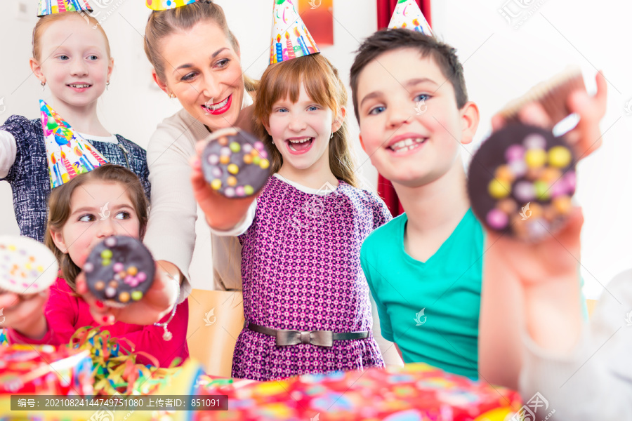 孩子们在生日派对上向镜头展示松饼蛋糕，更多的孩子和妈妈