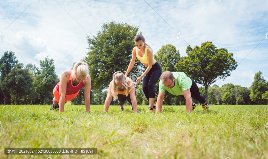 在草地上由健身教练指导下，一家人在大自然中做俯卧撑