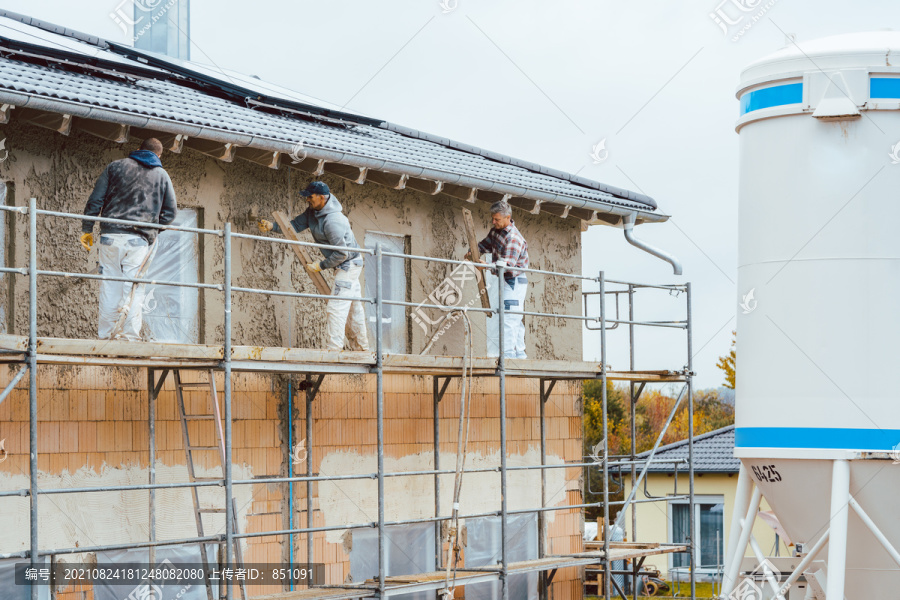 在房屋外墙上工作的脚手架上抹灰工人