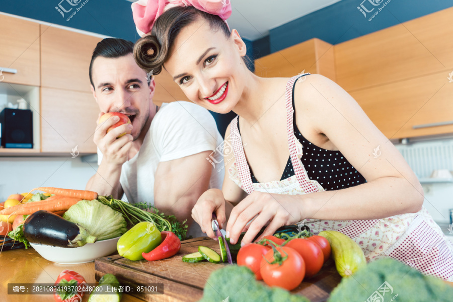 一个相当懒的男人一边吃苹果一边看着他的妻子准备食物