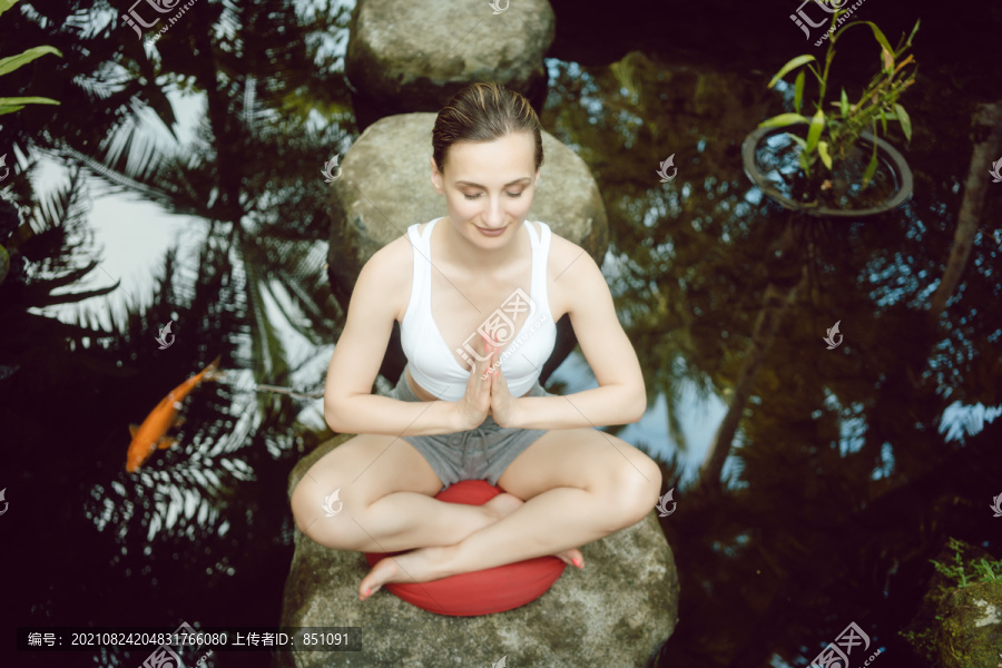 在池塘边练瑜伽的女人，金鱼坐在石头上