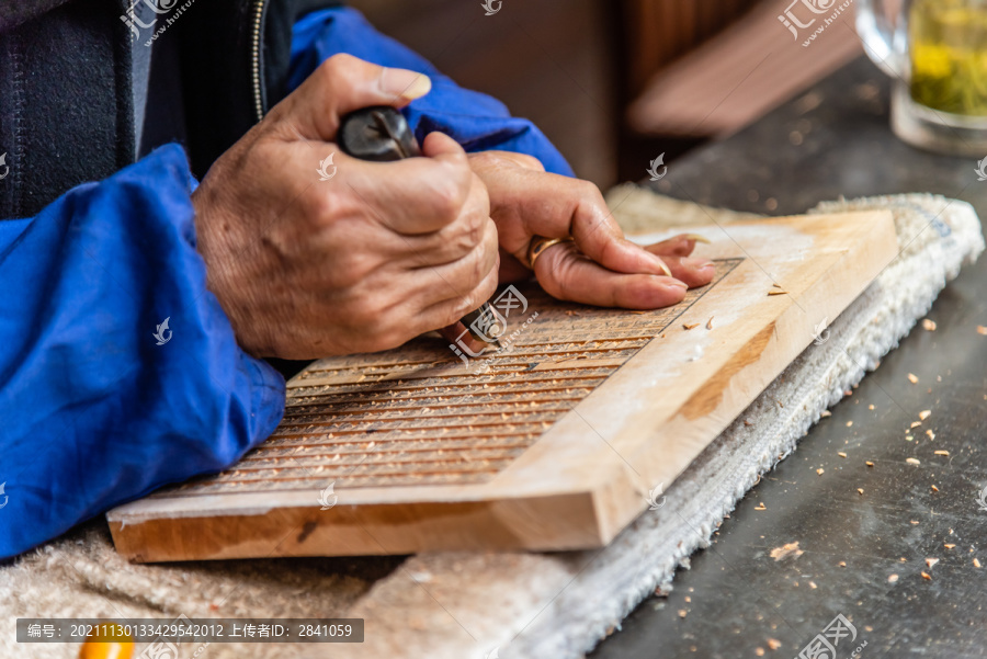 老人手拿着刻刀在木板上雕刻版雕