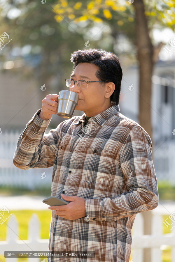 一个老年男人站在露营院子里拿着手机喝咖啡