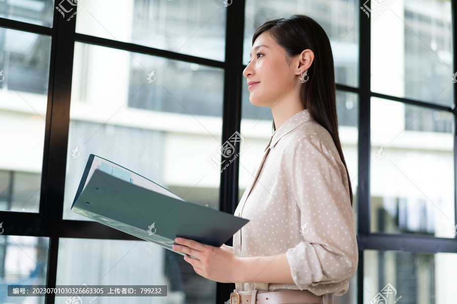一个商务女士站在落地窗前看文件