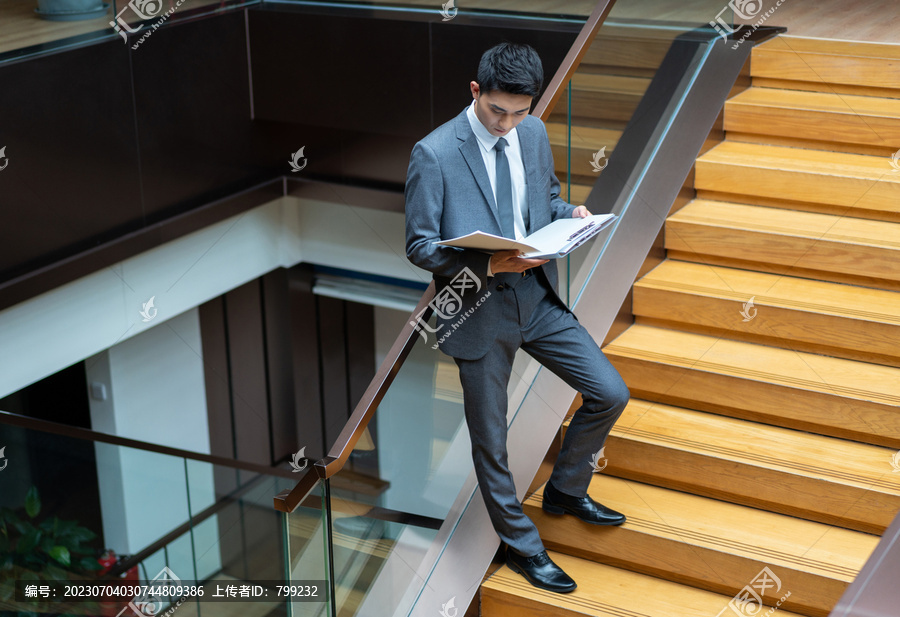 西装男士靠在楼梯上看文件