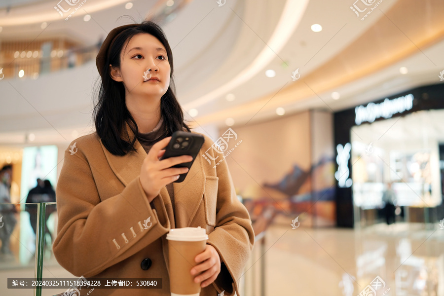 商场里年轻女性手持手机凝视思考