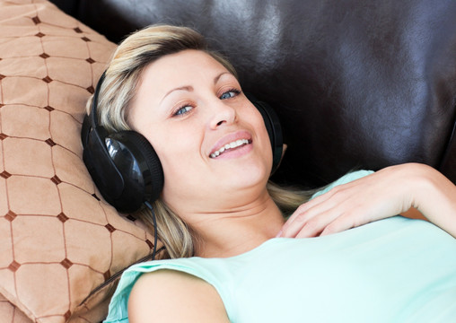 年轻的女人躺在沙发上听音乐