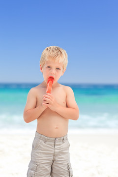 小男孩在海滩上吃棒冰