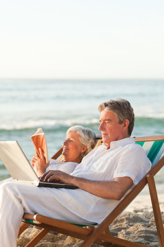 海边度假看书玩电脑的夫妇