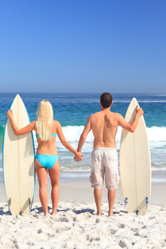 情侣拿着冲浪板在沙滩上