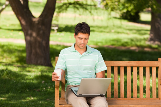 坐在公园长椅上玩电脑的男人
