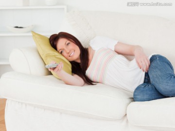 女人手拿遥控器躺在沙发上