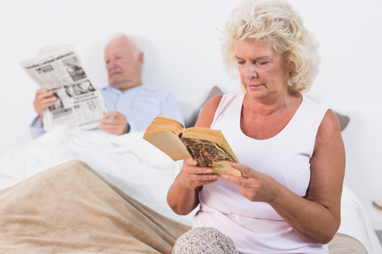 在卧室读书看报的老年夫妇
