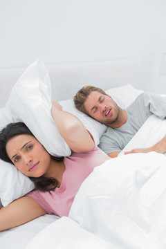 丈夫正在打鼾女人用枕头捂着耳朵