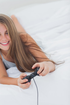 年轻女孩趴在床上玩电子游戏