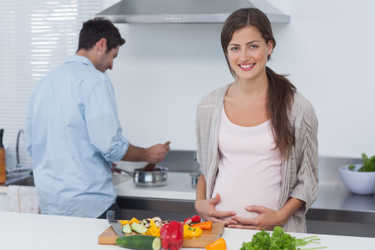 怀孕的女人抱着她的肚子在厨房里