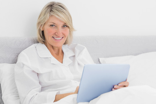 微笑的女人坐在床用平板电脑