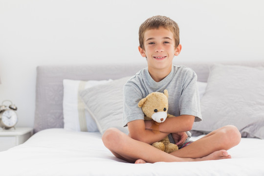 小男孩抱着泰迪熊坐在床上