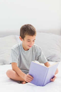 小男孩坐在家里的床上看书