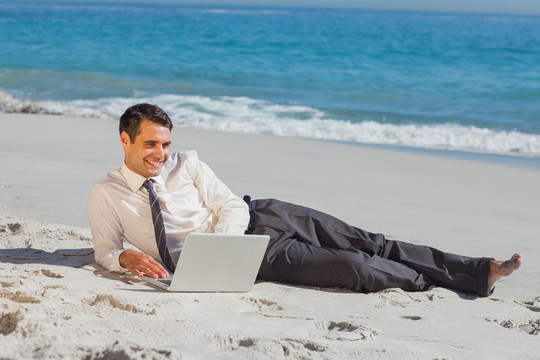 在沙滩上用笔记本电脑的男人