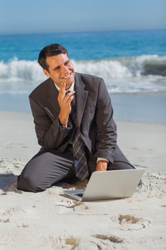 微笑的商人坐在沙滩上用电脑